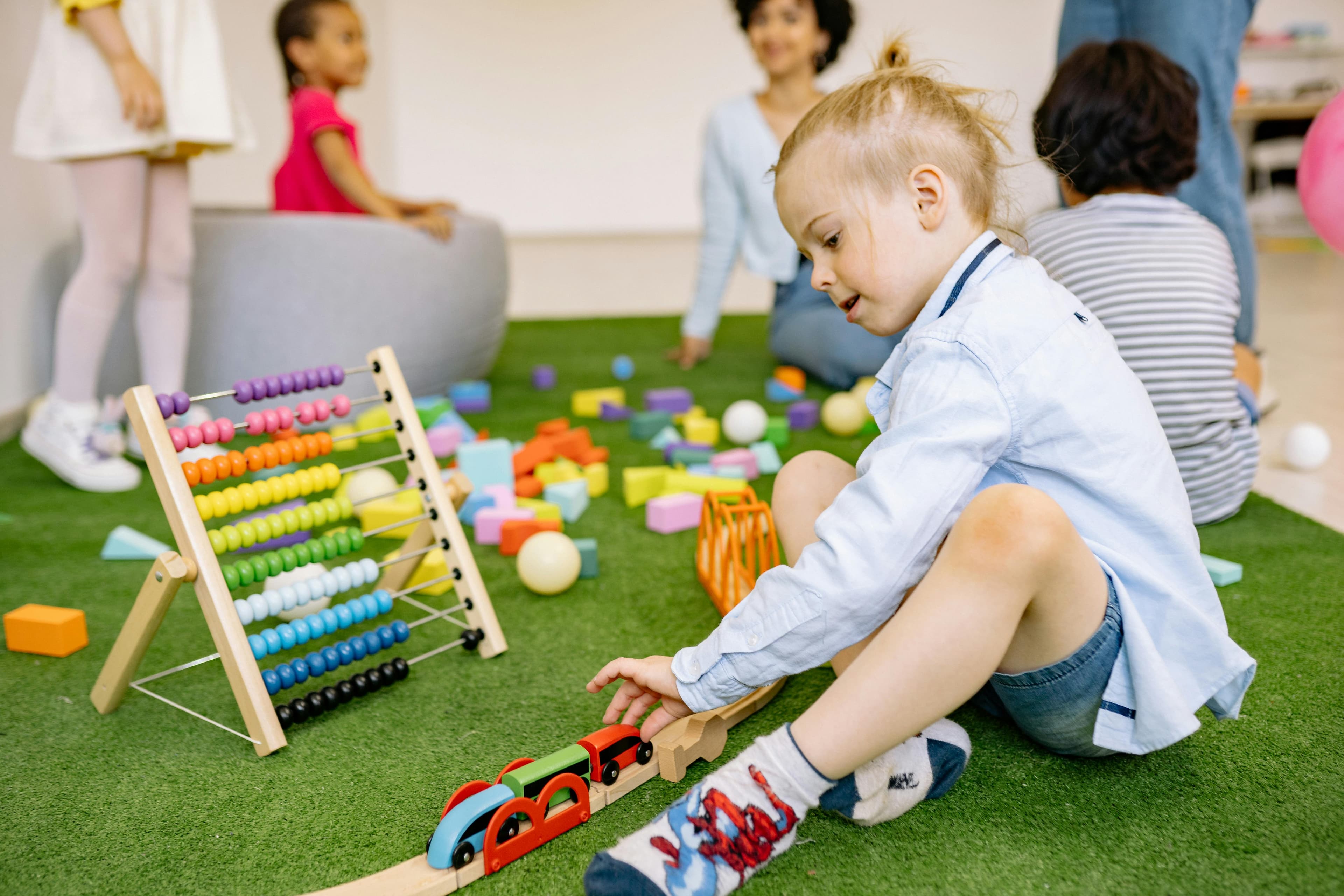 A group of young children playing with blocks, a model train, and a bead toy.