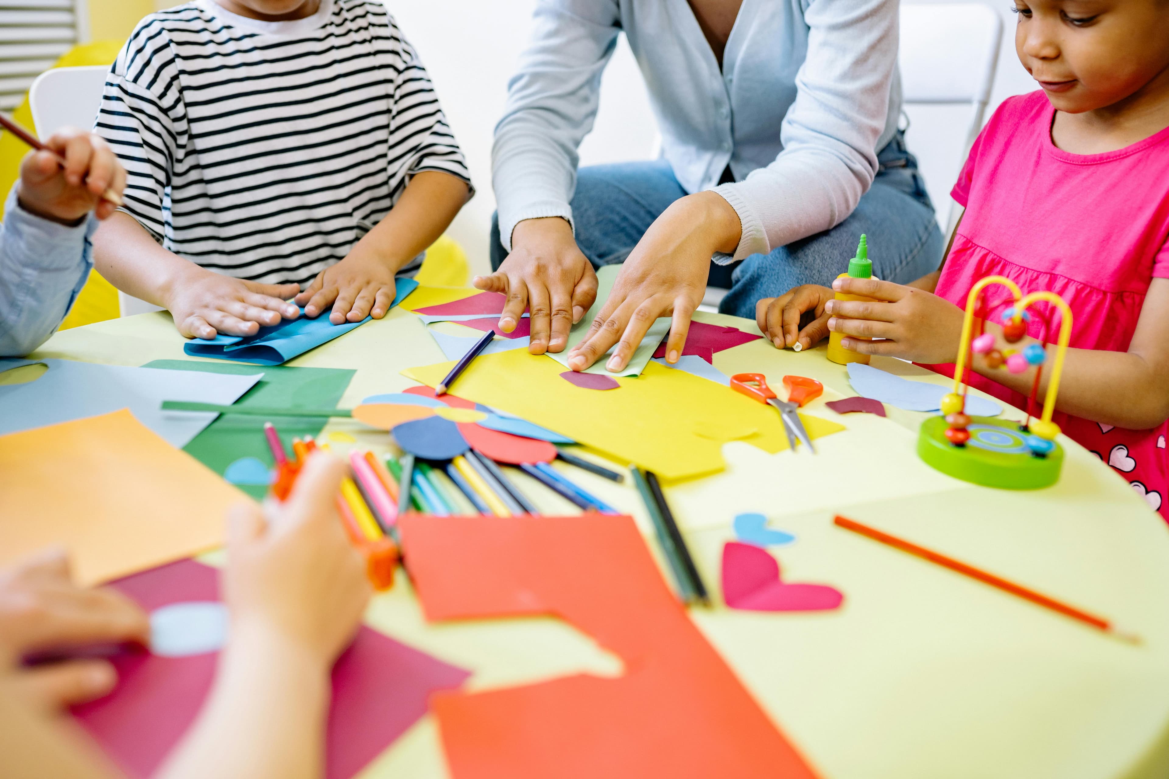 A pile of colorful paper and markers with children sitting around it crafting.