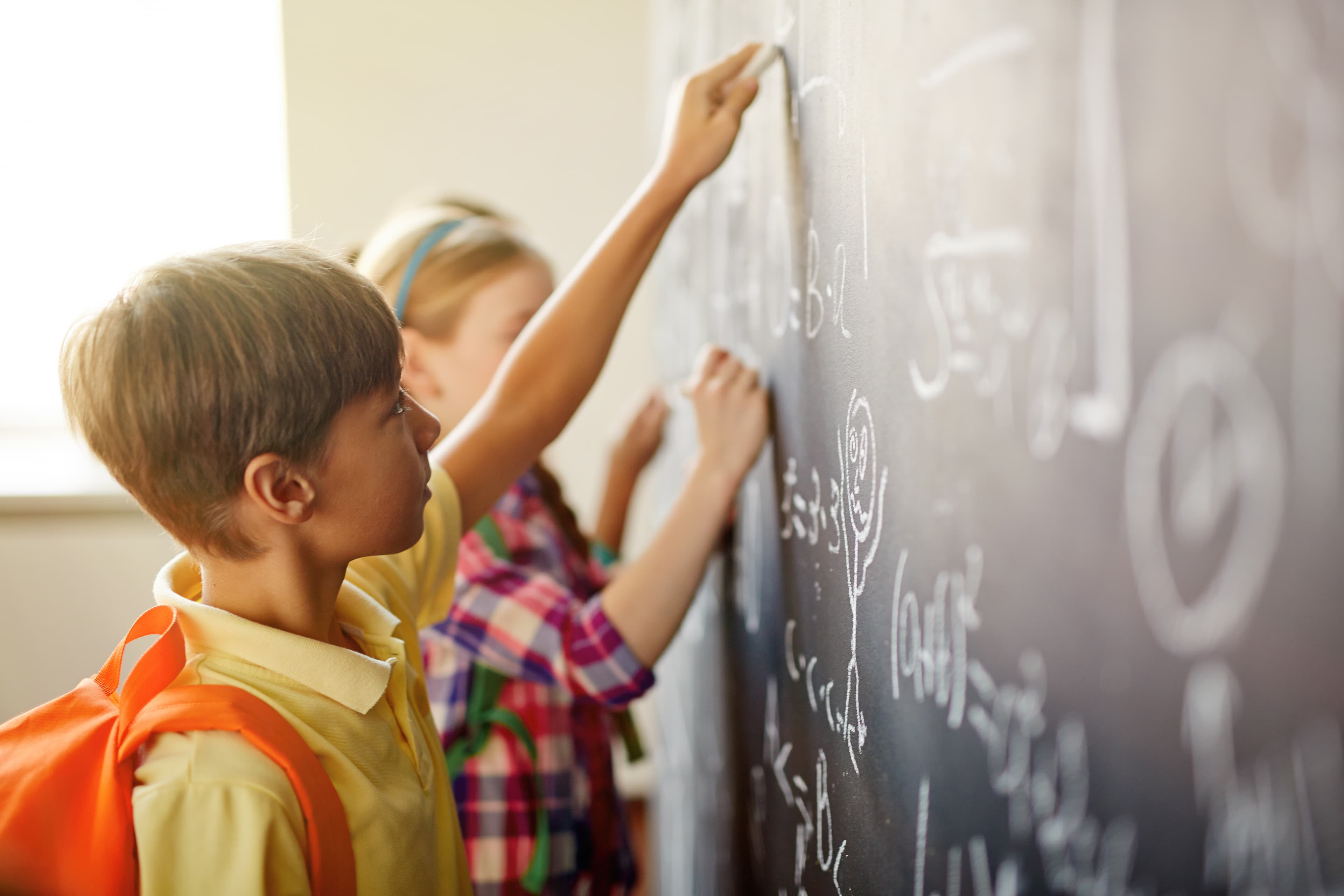 Children writing on a chalkboard in a classroom.